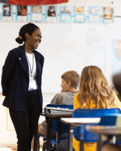 African american student of teachers for the nations smiling at the front of a classroom of students.